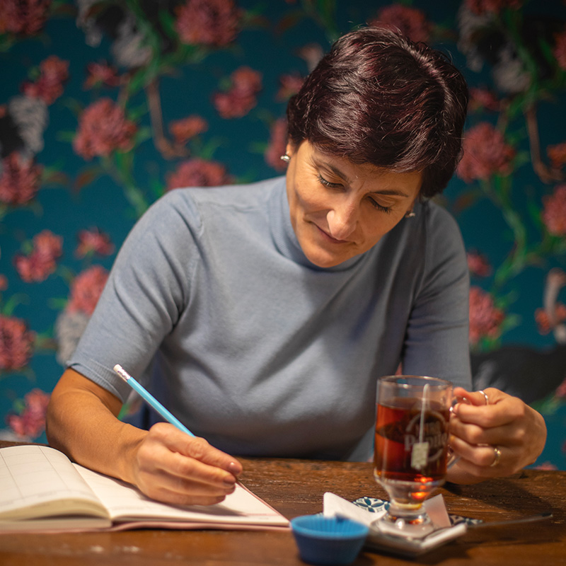 donna seduta che scrive con in mano una tazza di tè